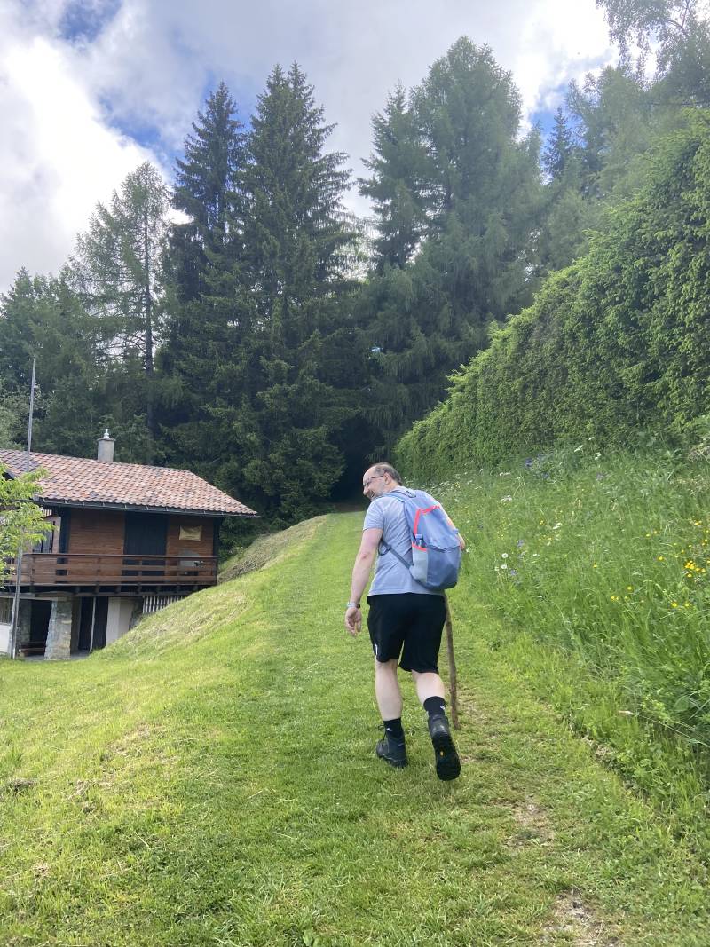 Moi en train de monter un chemin fait d’herbe rase, une haute haie sur la droite, un chalet sur la gauche