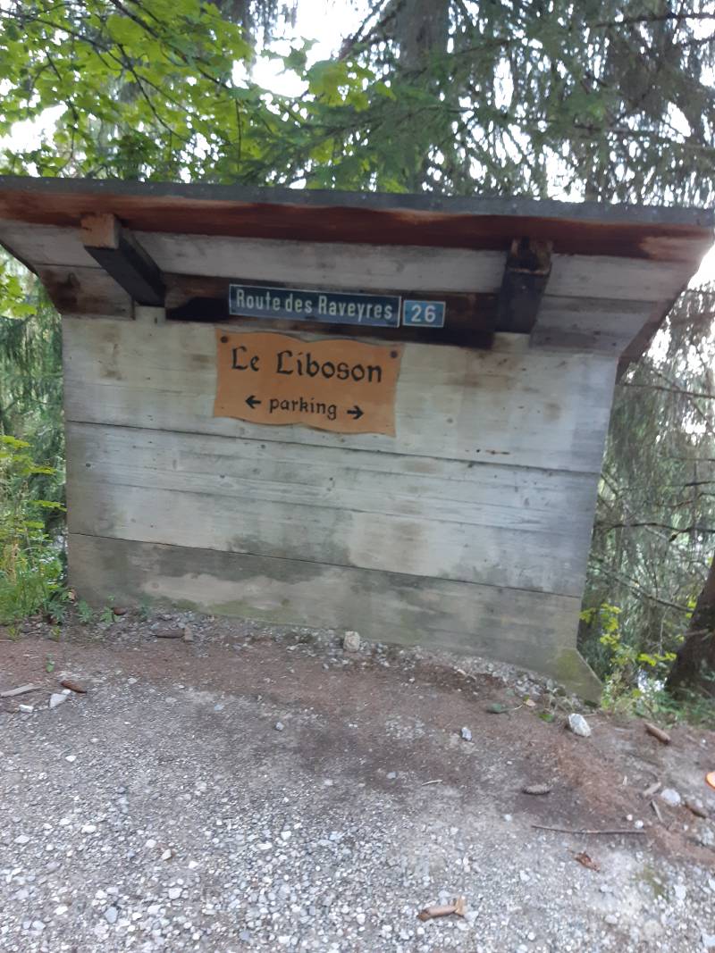 Petit abri en bois avec une pancarte “Route des Raveyres 26” et une autre “Le Liboson / parking”