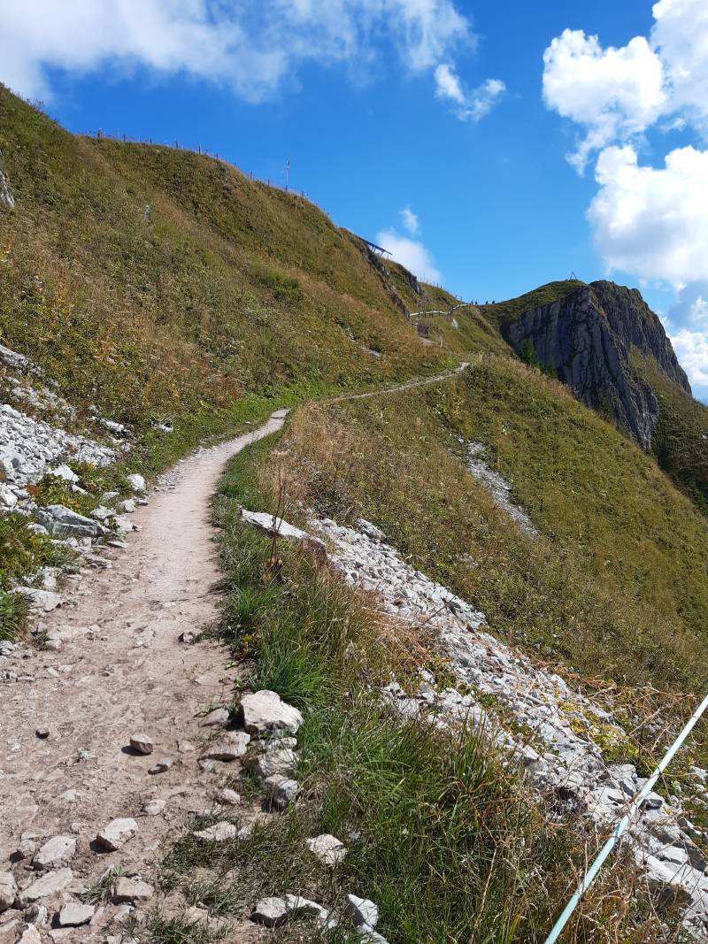 Petit chemin sinueux de terre sèche montant sur environ 100m; au bout, on aperçoit des silhouettes.