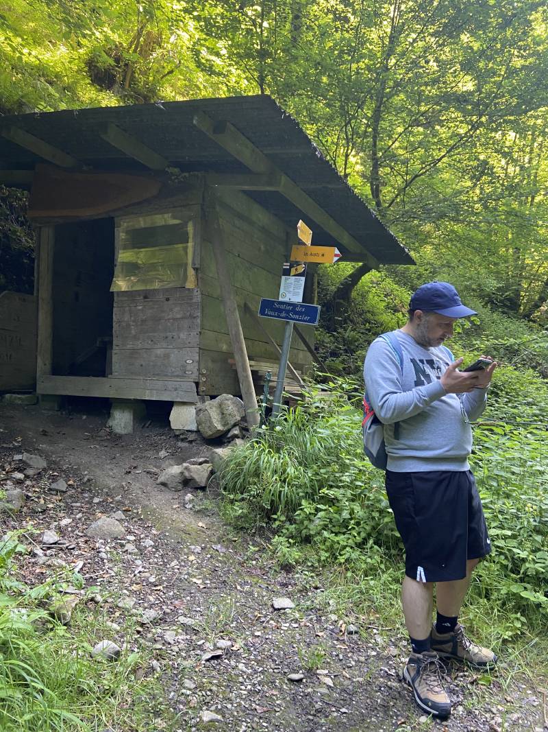 JF Poilprêt, portant short, sweat-shirt, casquette, sac à dos et chaussures de randonnée, en train de consulter la carte sur le smartphone, au lieu-dit ‘sentier des Vaux-de-Sonzier’ à mi-chemin