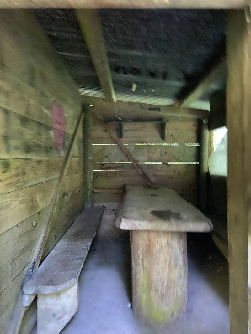 Une petite cabane, avec un banc et une table en bois, ouverture sur la droite.