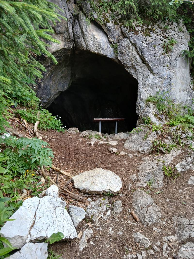 Large entrée d’une grotte dans la montagne, avec une petite table à l’intérieur.