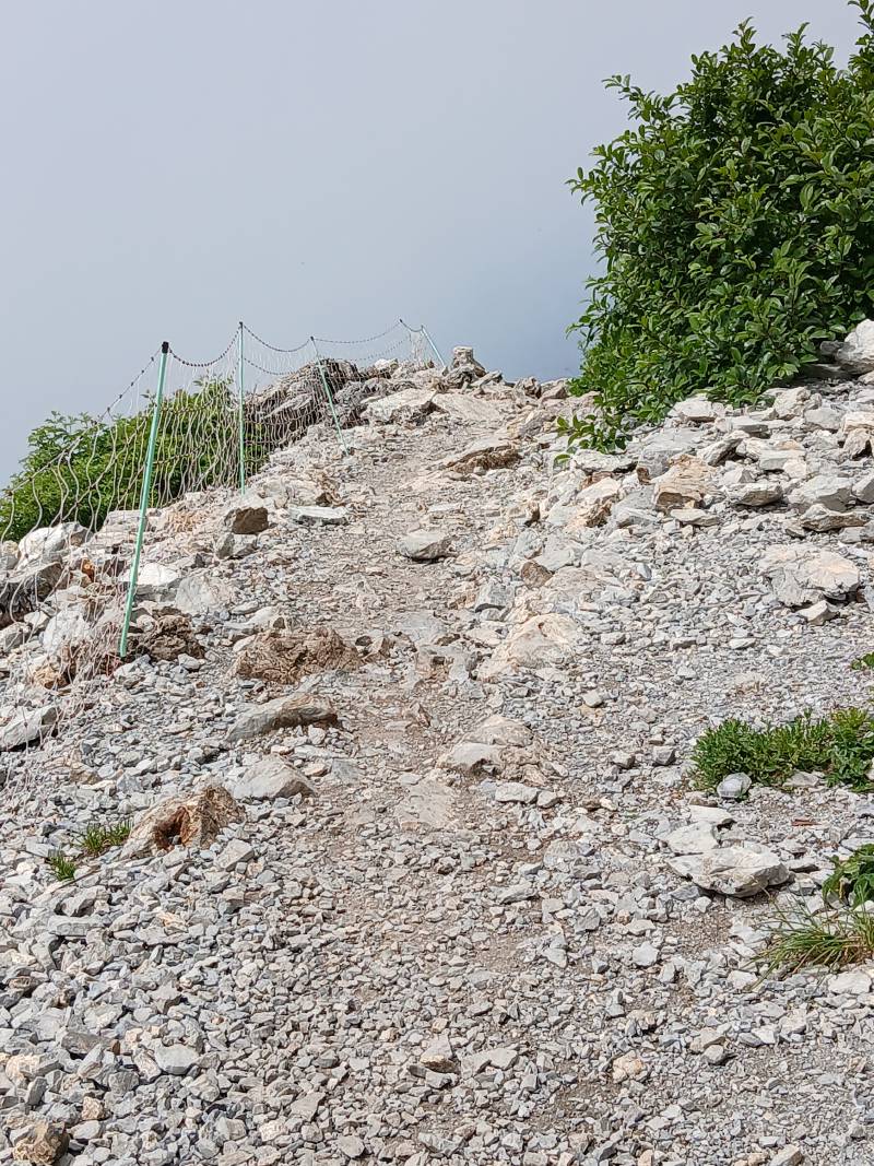 Vue sur un chemin fait de pierres de toutes tailles, avec le filet de protection sur la gauche cette fois-ci.
