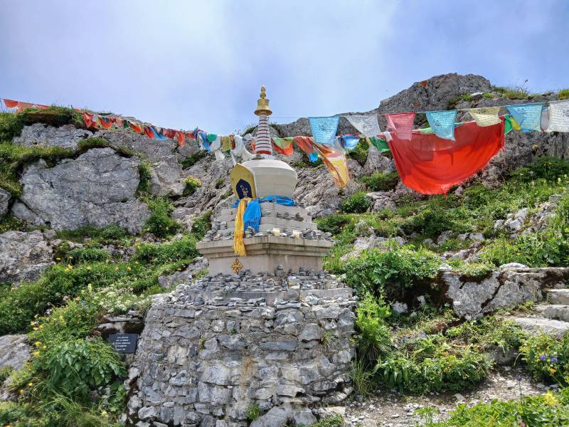 Stupa d’environ 3m de haut, construit contre la roche, des fanions multicolores sont suspendus à une corde partant du Stupa vers la droite, puis revenant sur la gauche. Au pied du Stupa se trouve une inscription “Stupa Himalayen érigé en souvenir du centième anniversaire de la Rambertia. Juillet 1996”