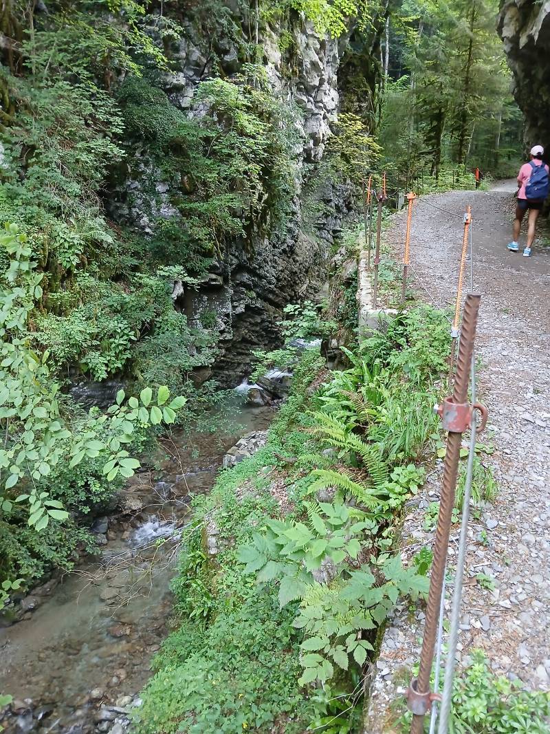 Petite route de graviers longeant la rivière sur la gauche, environ 1 mètre en dessous, le long du’une paroi rocheuse grisâtre