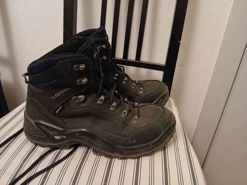 Une paire de chaussures de randonnées mi-hautes, posées sur une chaise. La marque LOWA apparaît, ainsi que le sigle “GORETEX”