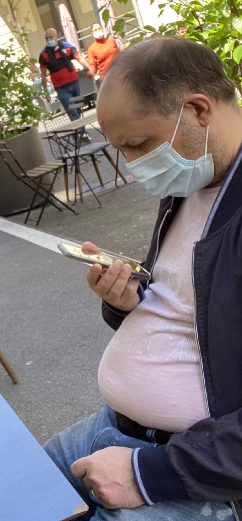 Moi, assis à une table de café, portant un masque chirurgical, en train d’observer mon smartphone